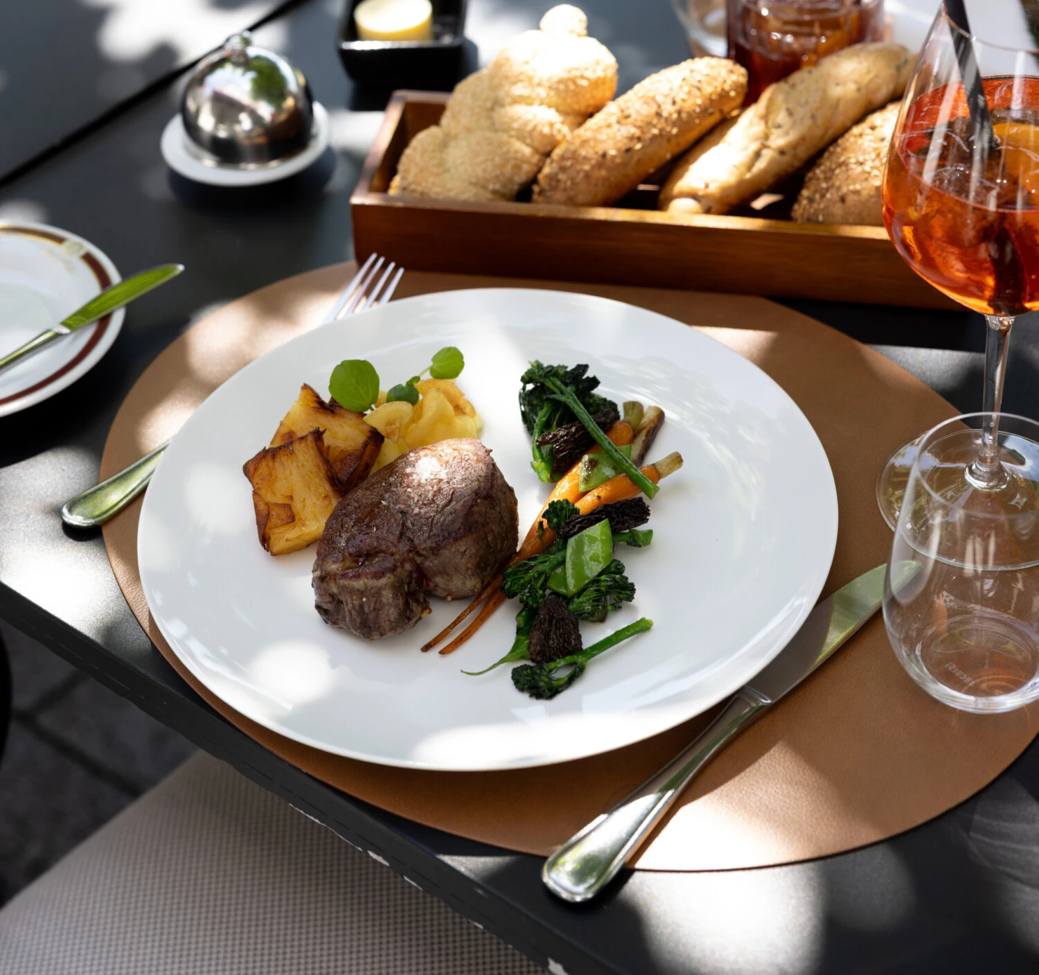 Feinstes Rinderfilet mit glasiertem Gemüse, Kartoffelgratin und Apfelpüree, serviert im eleganten Außenbereich mit Brotkorb und Aperitif.