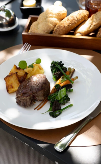 Feinstes Rinderfilet mit glasiertem Gemüse, Kartoffelgratin und Apfelpüree, serviert im eleganten Außenbereich mit Brotkorb und Aperitif.