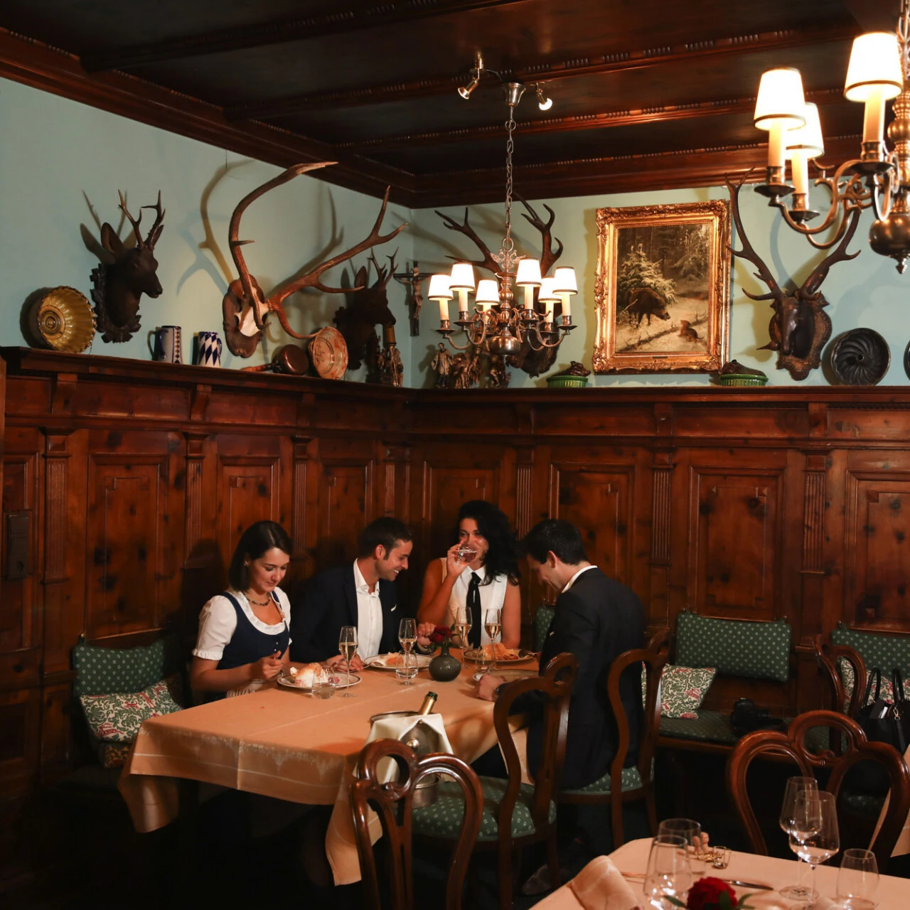 Gemütliches Dinner in rustikalem Ambiente mit Holztäfelung, Jagdtrophäen und fröhlicher Runde bei Dessert und Wein.