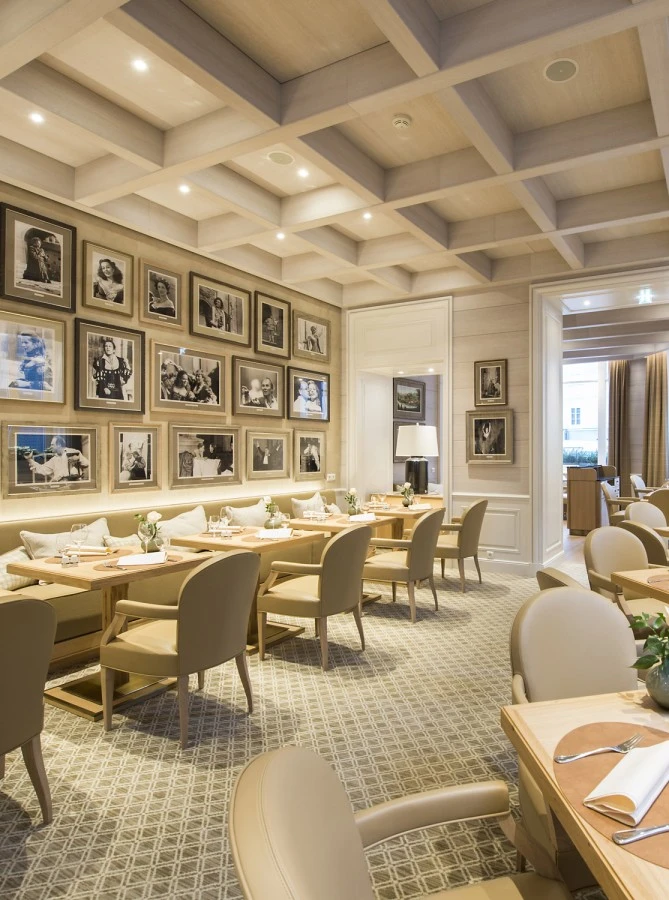 Heller, moderner Restaurantbereich mit gemütlicher Atmosphäre. Die Rückwand ist dekorativ mit zahlreichen schwarz-weißen Porträts berühmter Persönlichkeiten in goldenen und schwarzen Rahmen geschmückt, die in drei Reihen angeordnet sind.