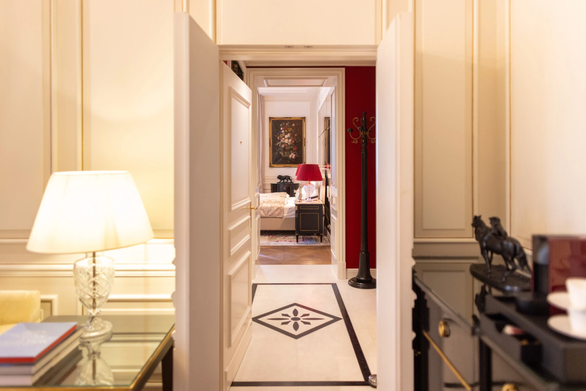 Blick durch geöffnete Flügeltüren auf ein stilvolles Schlafzimmer mit roten Wänden, klassischem Mobiliar und floraler Wandkunst.