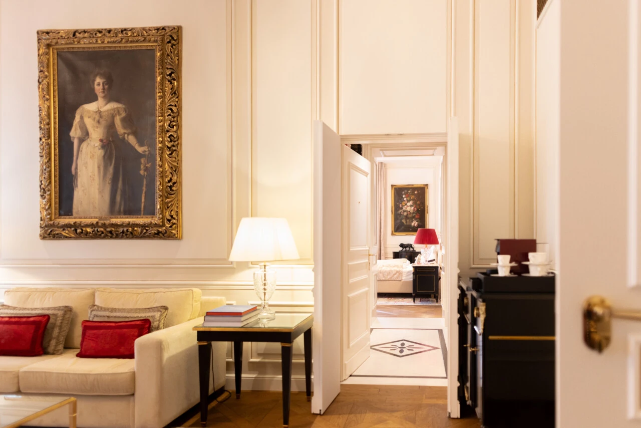 Eleganter Wohnbereich mit klassischem Porträt, beiger Couch und Blick in ein stilvoll eingerichtetes Schlafzimmer mit roter Akzentbeleuchtung.