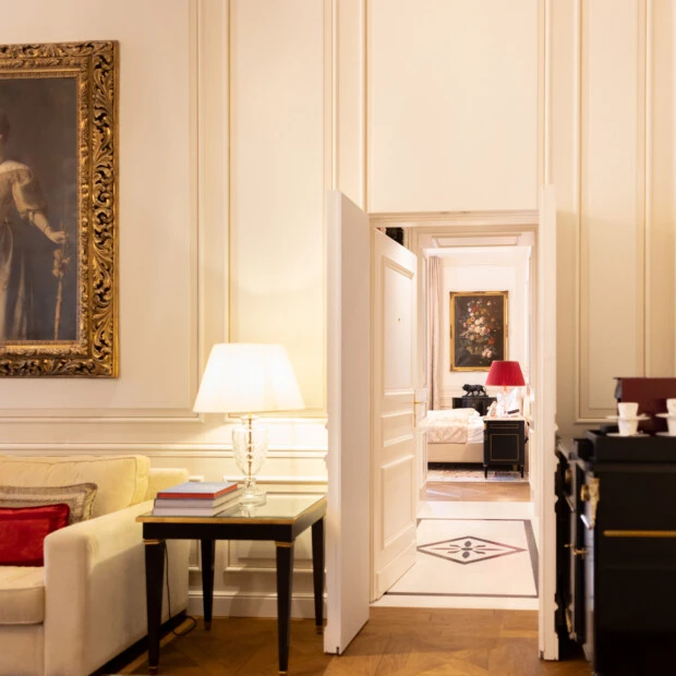 Eleganter Wohnbereich mit klassischem Porträt, beiger Couch und Blick in ein stilvoll eingerichtetes Schlafzimmer mit roter Akzentbeleuchtung.