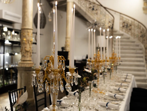 SacherxLobmeyr-Dinner-6 Prächtig gedeckter Festsaal mit langer Tafel, goldenen Kerzenleuchtern, hoher Decke und geschwungener Treppe im Hintergrund.