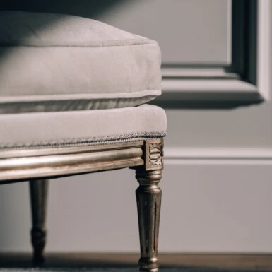 Eine Nahaufnahme eines eleganten Stuhls im klassischen Stil, der durch seinen weichen Stoff und die verzierten, vergoldeten Beine besticht.