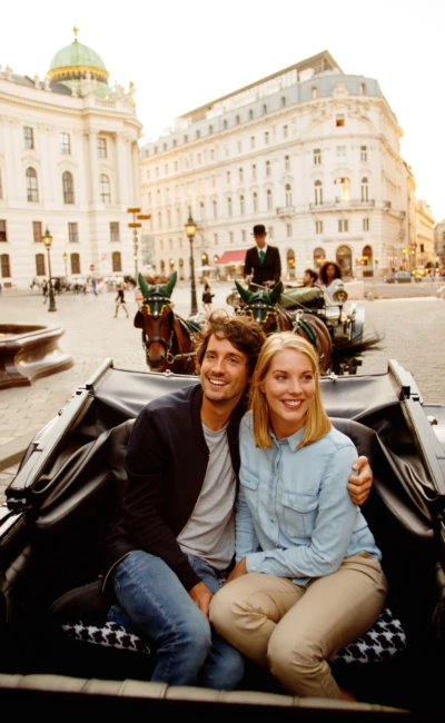 Lächelndes Paar bei einer Fiakerfahrt durch die Wiener Innenstadt vor der Hofburg
