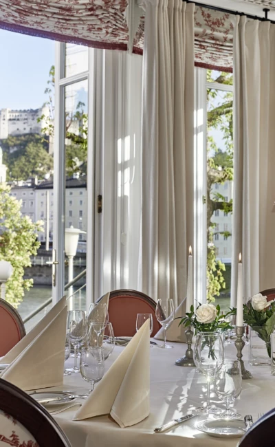 Festlich gedeckter Restauranttisch mit Kerzen und weißen Rosen mit Blick auf die Festung Hohensalzburg in Salzburg