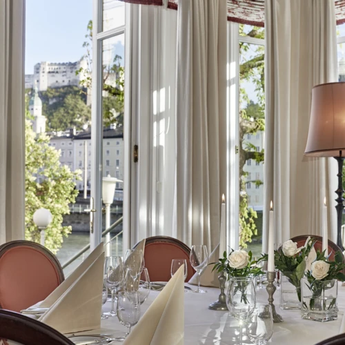Festlich gedeckter Restauranttisch mit Kerzen und weißen Rosen mit Blick auf die Festung Hohensalzburg in Salzburg