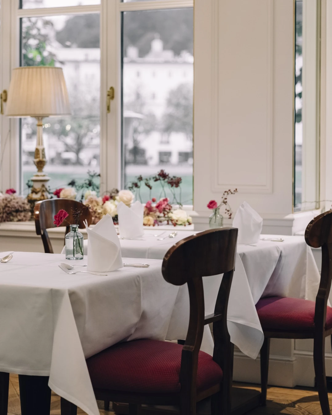 Gemütliches Event-Raum mit Blumenfensterbank, weißen Tischdecken und nostalgischen Tischlampen