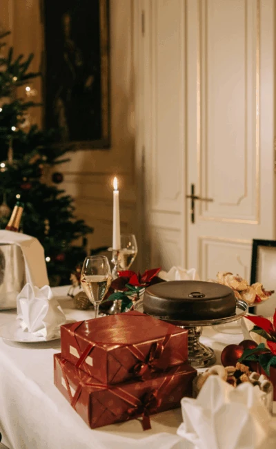 Ein festlicher Weihnachtstisch mit verpackten Geschenken, Kerzen und Weihnachtssternen, vor dem Hintergrund eines geschmückten Weihnachtsbaumes und eines eleganten Zimmers.