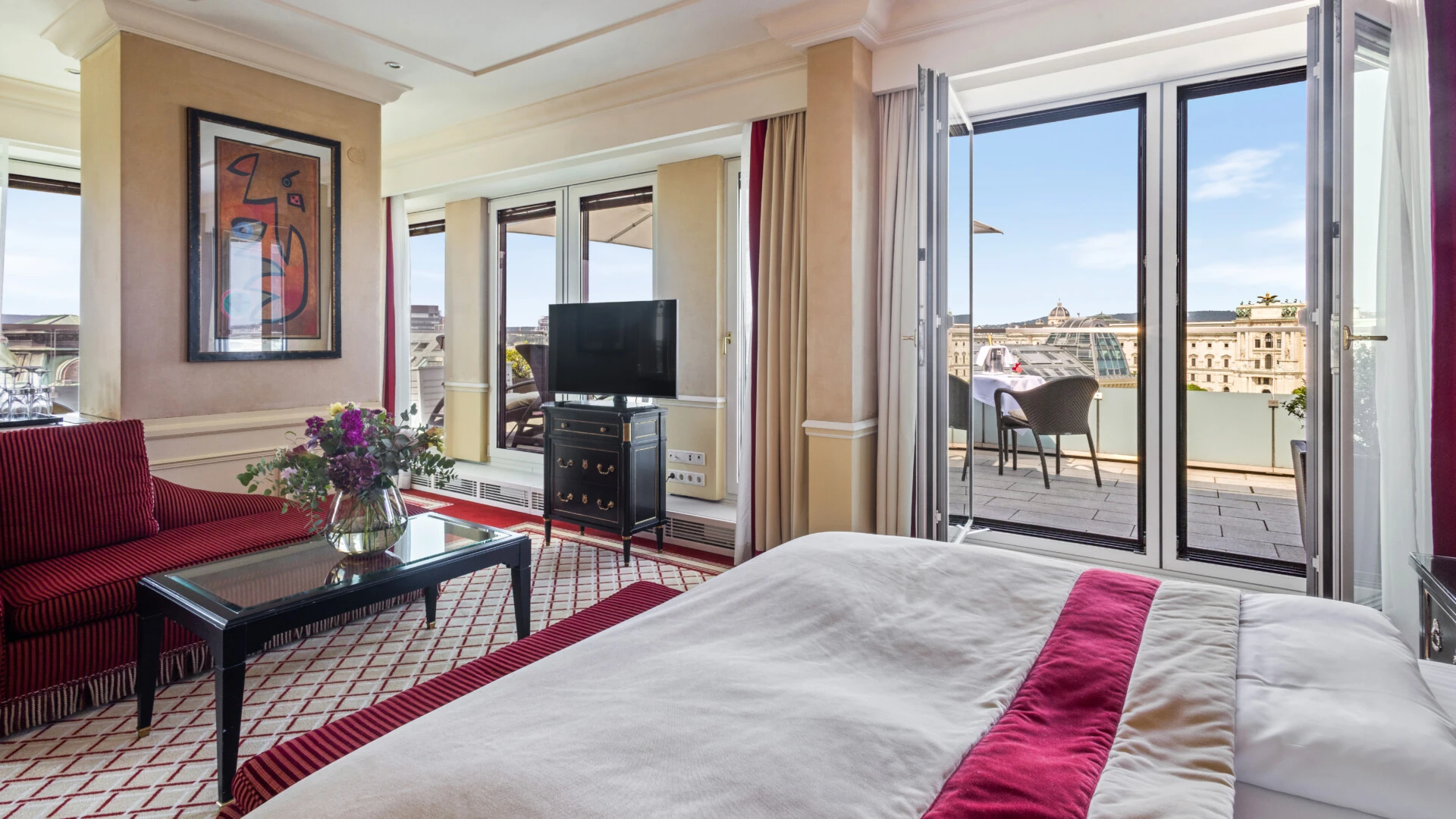Ein geräumiges Hotelzimmer mit einem bequemen Bett und einer privaten Terrasse, von der aus man einen atemberaubenden Panoramablick über die Dächer der Stadt genießen kann.