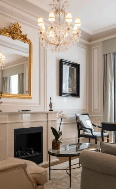 Ein klassisches Wohnzimmer mit Kamin, verziertem Goldspiegel, Kristallleuchter und eleganten antiken Möbeln.