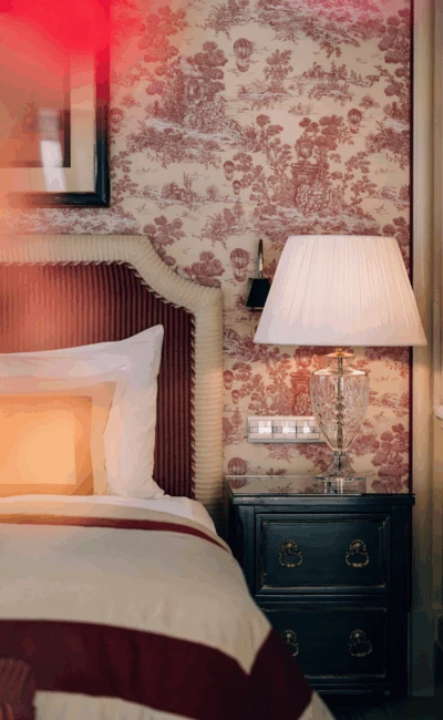 Ein gemütliches Hotelzimmer mit einem Bett, rot-weißer Toile-Tapete und einem Nachttisch mit Lampe.