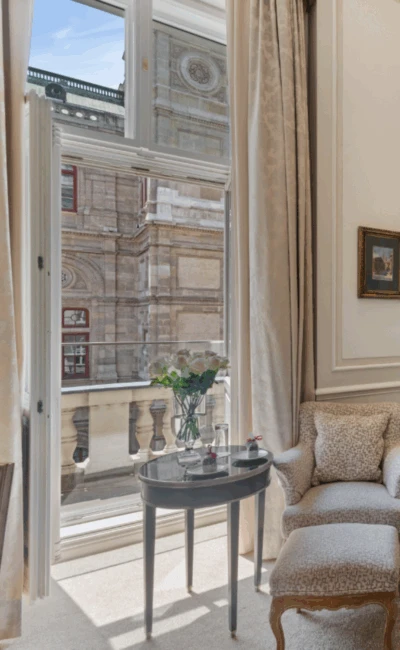 Ein wunderschönes Hotelzimmer mit einem Bett, eleganter Einrichtung und einem atemberaubenden Blick vom Balkon auf die Wiener Staatsoper.