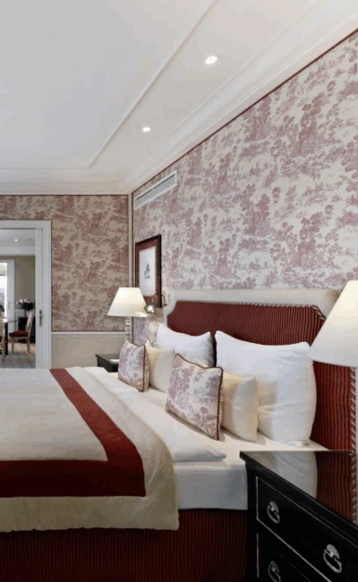 Ein luxuriöses Hotelzimmer mit einem Bett, roter Toile-Tapete und einer großen offenen Tür zum Esszimmer.