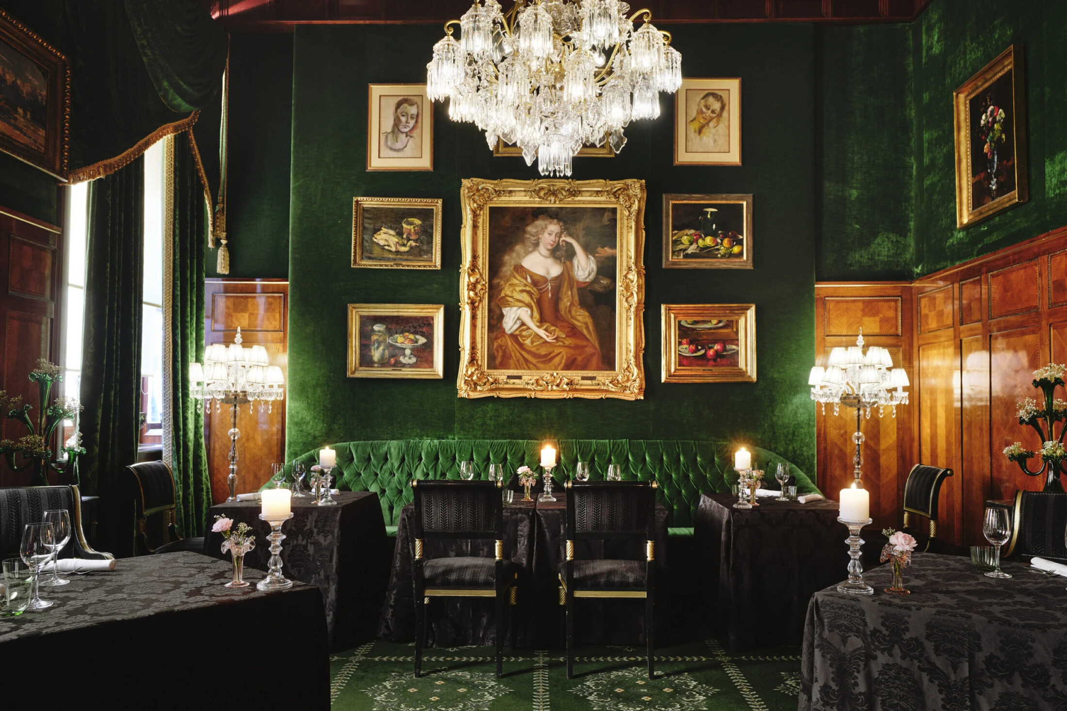 Opulenter, grün getäfelter Speisesaal mit Gemälden, Kristallleuchter und Kerzenlicht.