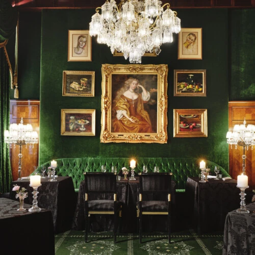 Opulenter, grün getäfelter Speisesaal mit Gemälden, Kristallleuchter und Kerzenlicht.