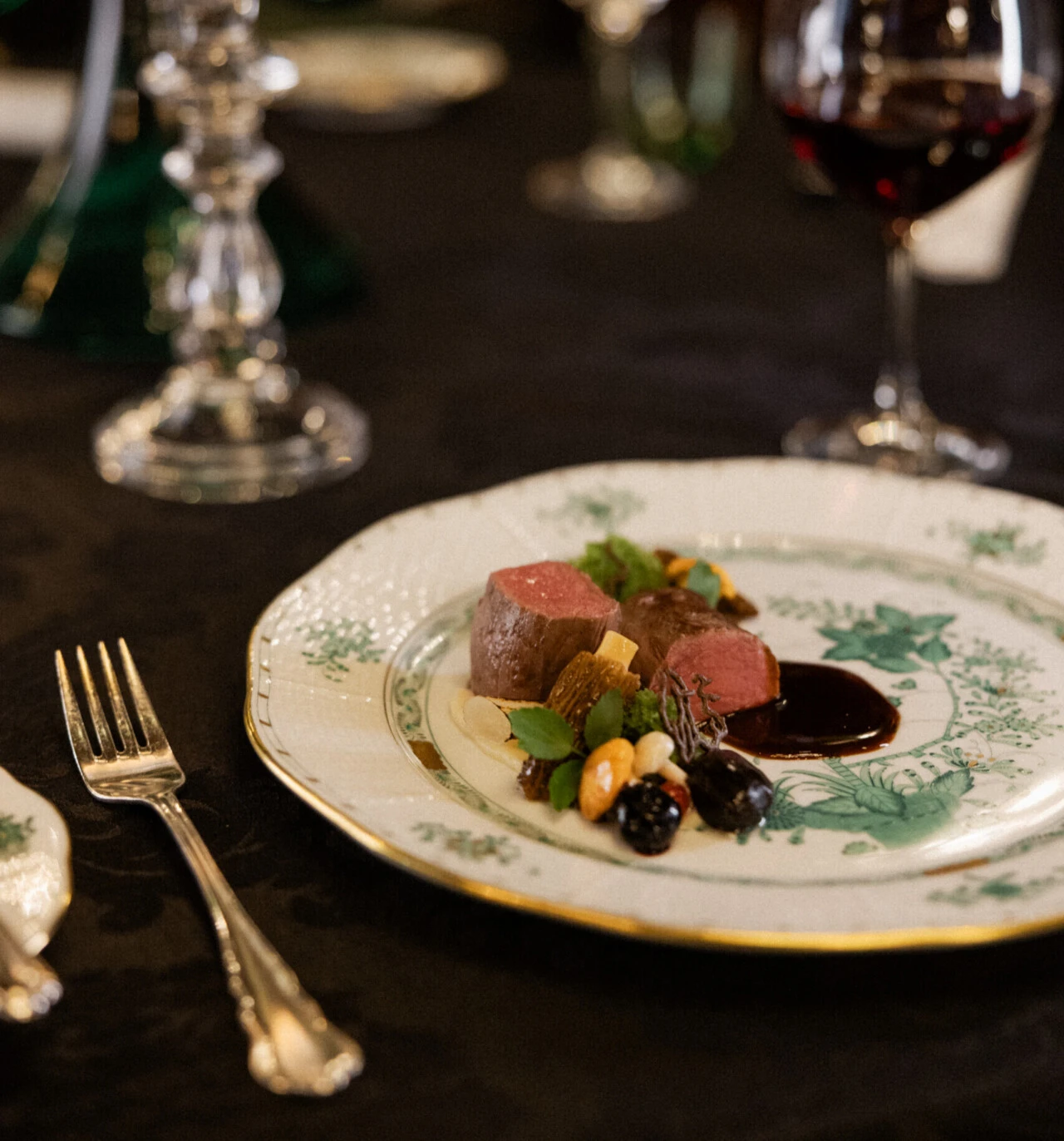 Hauptgang mit rosa gebratenem Fleisch, Gemüse und dunkler Sauce auf elegantem Teller.