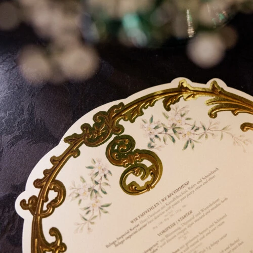 Nahaufnahme einer dekorativen Menükarte mit goldenen Ornamenten auf dem Tisch.
