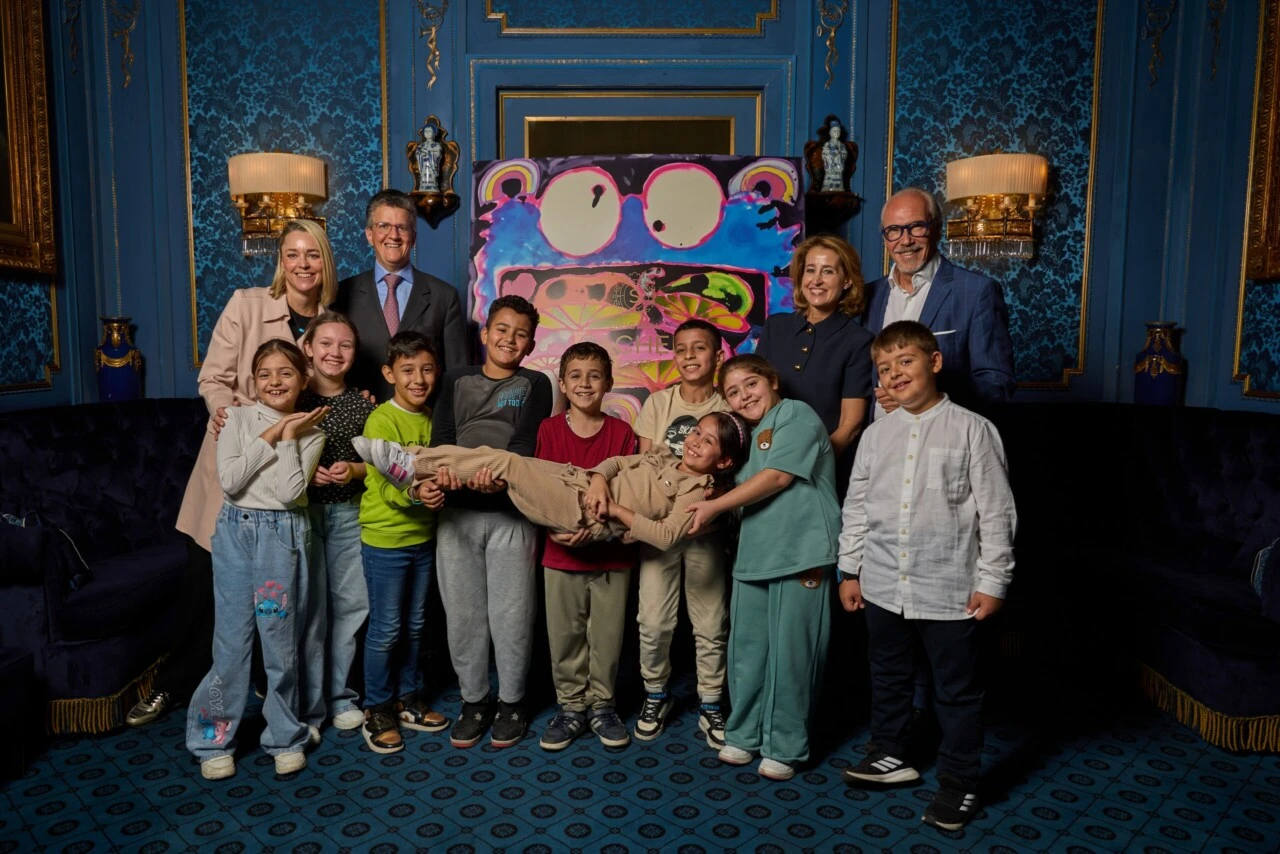 Gruppenfoto des Sacher-Teams mit Kindern und dem farbenfrohen Kunstwerk der Limited Edition 2025 im Hintergrund
