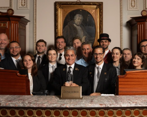 Eine große Gruppe von Hotel-Concierges, lächelnd hinter einem Tresen, mit einem „Concierge“-Schild in der Mitte.