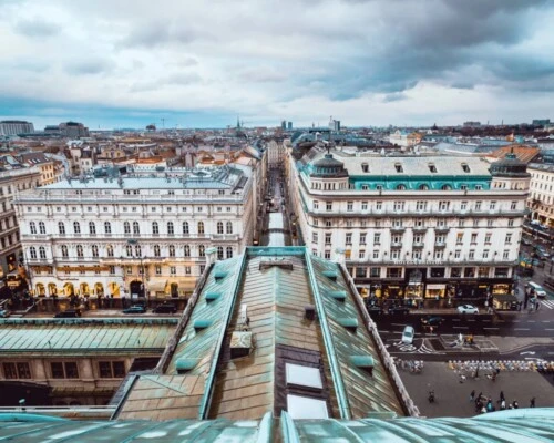 Eine Aufnahme aus der Vogelperspektive über die Dächer und Straßen von Wien, Österreich, mit historischen Gebäuden unter einem bedeckten Himmel.