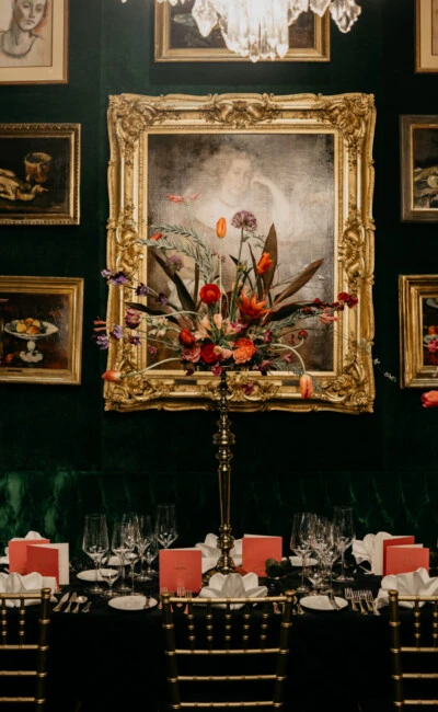 Langer Tisch, gedeckt für ein formelles Gala-Dinner in einem luxuriösen Raum mit dunkelgrünen Samtwänden, Kronleuchtern und hohen Blumenarrangements.