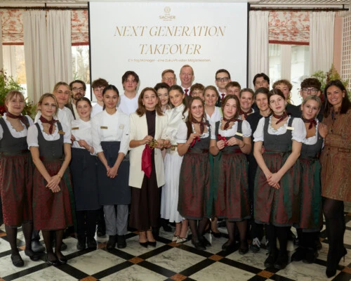 Eine große Gruppe von Hotelmitarbeitern und Studierenden posiert unter einem „Next Generation Takeover“-Banner in einem eleganten Raum.