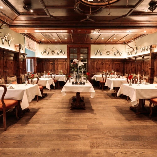 Traditionelles Zirbelzimmer Restaurant mit edler Holzvertäfelung, Geweih-Dekor und weiß gedeckten Tischen.