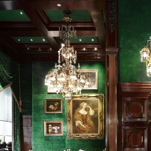 Prunkvoller Raum mit smaragdgrüner Stoffbespannung, kunstvoll drapierten Vorhängen und goldenen Troddeln. An den Wänden hängen klassische Gemälde in goldenen Rahmen.