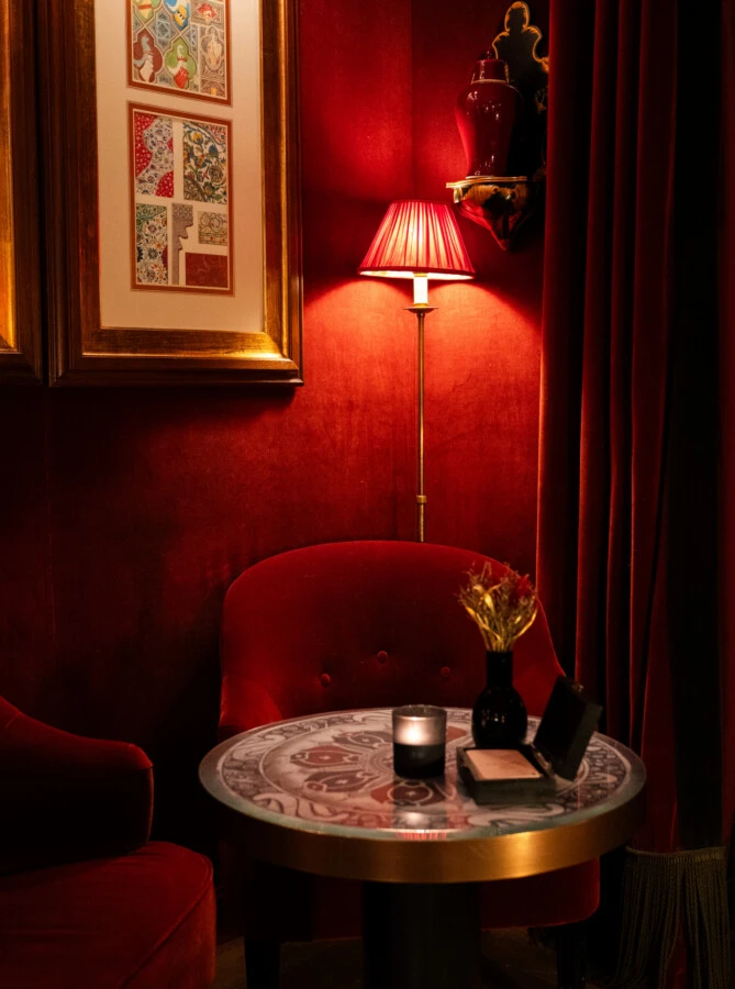 Elegant beleuchtete Hotel-Lounge mit roten Samtwänden, Sessel und einem runden Marmortisch.