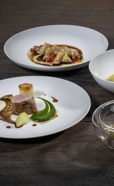 Sechs Teller mit fein angerichteten Gerichten auf einem dunklen Holztisch