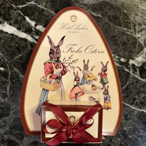 Ovale Sacher Osterverpackung mit nostalgischen Hasenillustrationen und roter Schleife auf Marmortisch