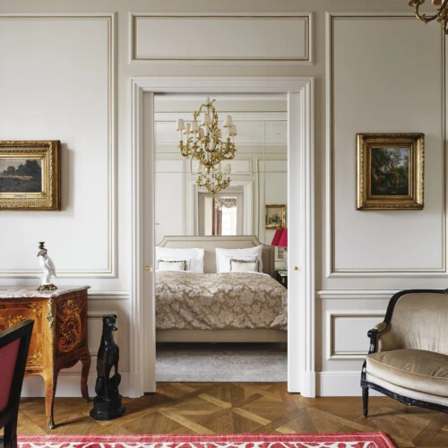 Eleganter Wohnbereich mit antiken Möbeln, goldgerahmten Gemälden und Blick durch die Tür in ein klassisch eingerichtetes Schlafzimmer