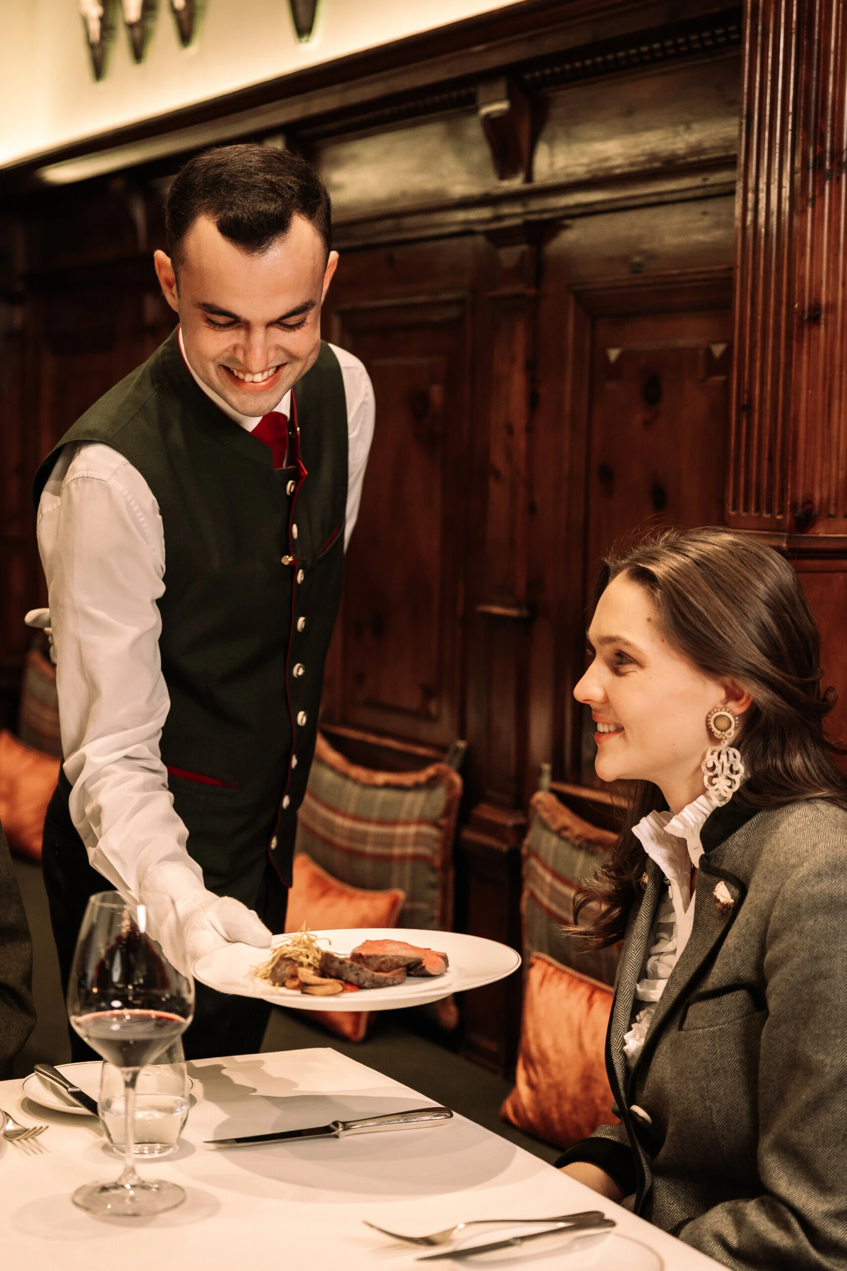 Restaurant Zirbelzimmer. Kellner serviert ein Gericht an eine Frau in traditionell-elegantem Restaurantambiente.