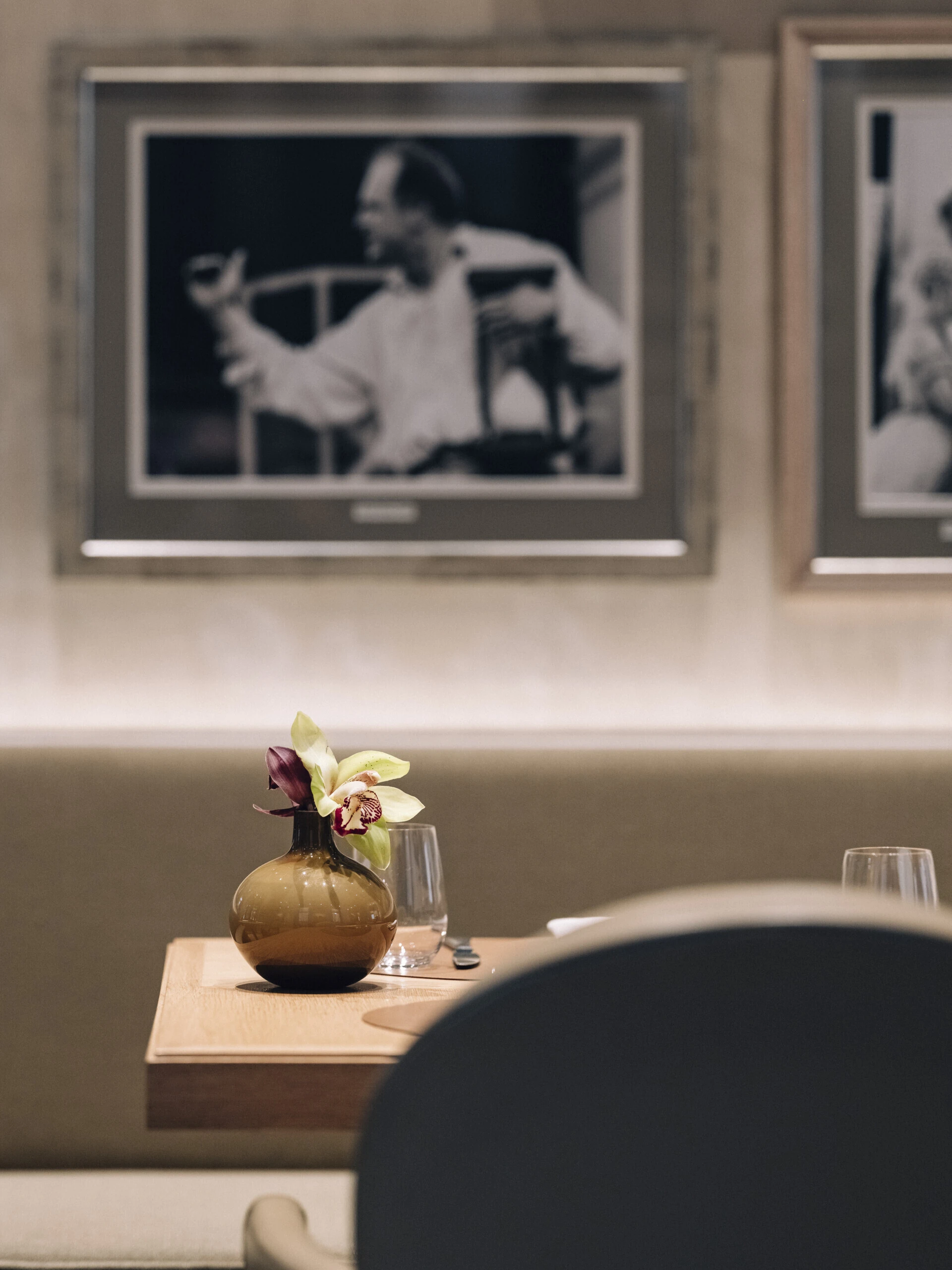 Elegantes Restaurant mit gemütlicher Atmosphäre. An den Wänden hängen zahlreiche Schwarz-Weiß-Porträts prominenter Persönlichkeiten, überwiegend aus Kunst und Kultur. Die Einrichtung ist geprägt von warmen Holztönen, bequemen Polsterstühlen und stilvoll gedeckten Tischen.