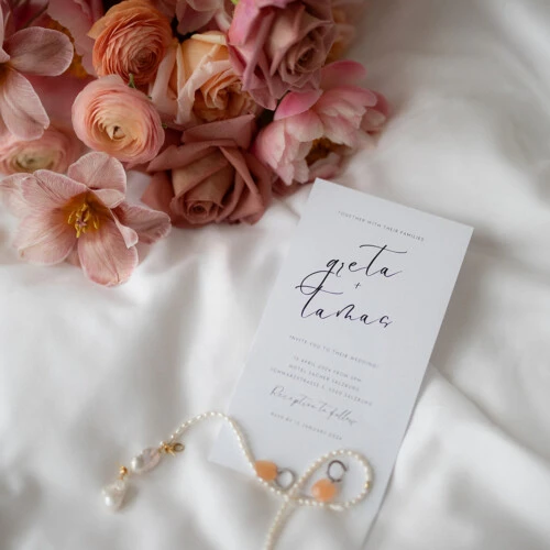Rosa Rosen und eine handbeschriftete Karte auf weißem Stoff als elegantes Detailarrangement