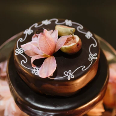 Original Sacher-torte mit glänzender Glasur, rosa Blütenblättern und filigraner weißer Verzierung.