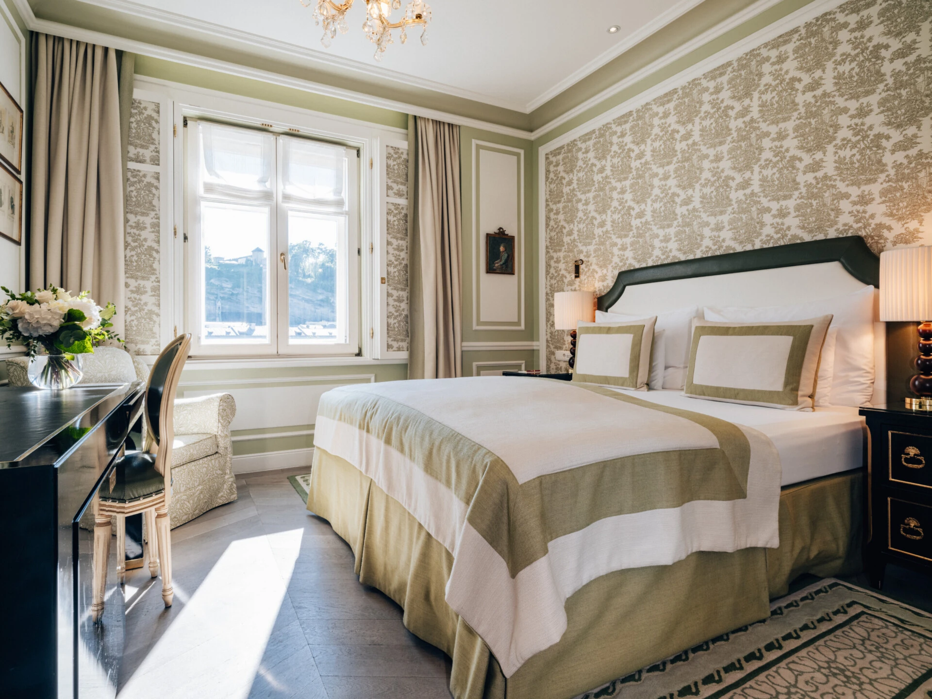 Deluxe Zimmer mit Ausblick im Hotel Sacher Salzburg mit Kingsize-Bett, elegantem Schreibtisch, klassischem Interieur und großen Fenstern mit Blick auf die Salzburger Altstadt