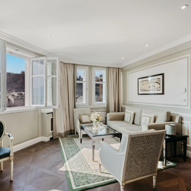Wohnbereich der Signature Suite mit Ausblick im Hotel Sacher Salzburg, mit eleganter Sitzecke, großen Fenstern und Blick auf Salzburg