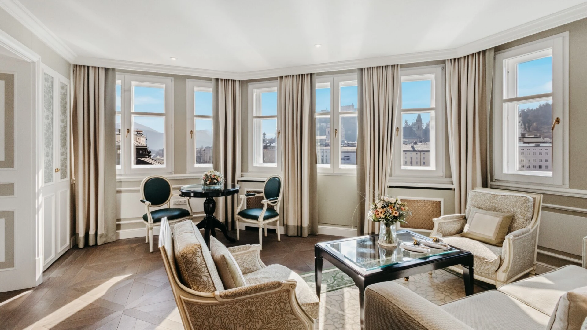 Heller Wohnbereich der Signature Suite mit Ausblick im Hotel Sacher Salzburg, mit klassischen Sesseln, Glastisch und Panoramafenstern