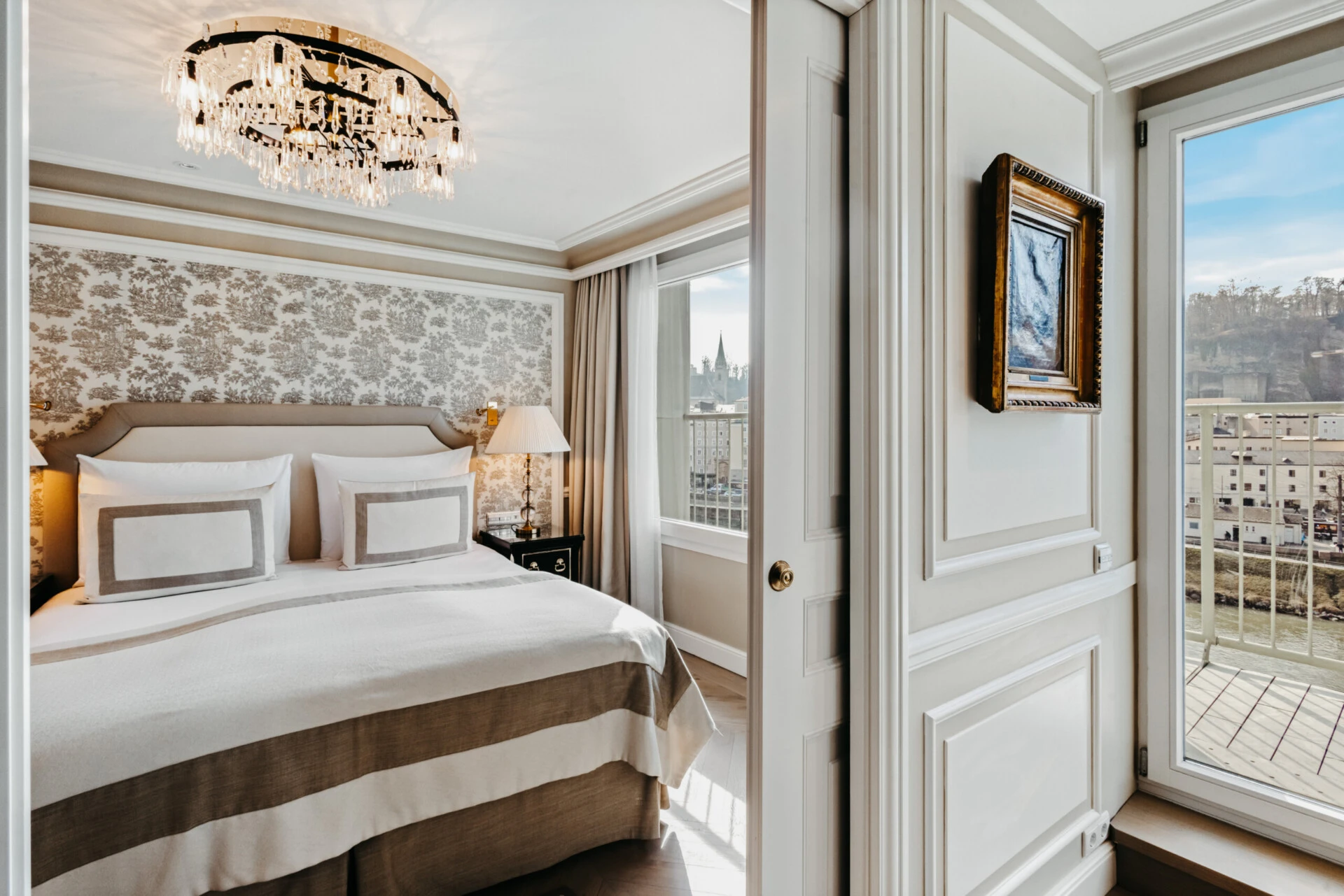 Schlafzimmer der Signature Suite mit Balkon im Hotel Sacher Salzburg, mit elegantem Bett, Kristalllüster und Balkonblick