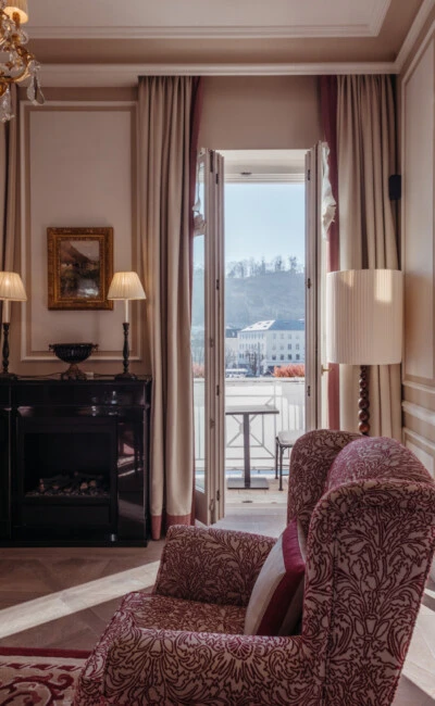 Familiensuite mit Ausblick im Hotel Sacher Salzburg, mit Schlafzimmer, Sitzbereich und eleganten roten Musterdetails