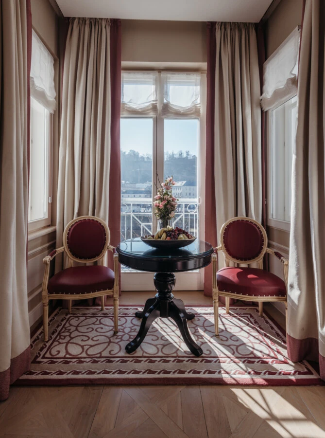 Sitznische der Familiensuite mit Ausblick im Hotel Sacher Salzburg, mit rundem Tisch, roten Stühlen und großen Fenstern