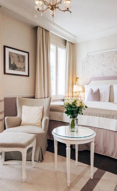Deluxe Zimmer im Hotel Sacher Salzburg mit elegantem Bett, Sitzbereich, frischen Blumen und klassischem Interieur in sanften Rosé- und Beigetönen