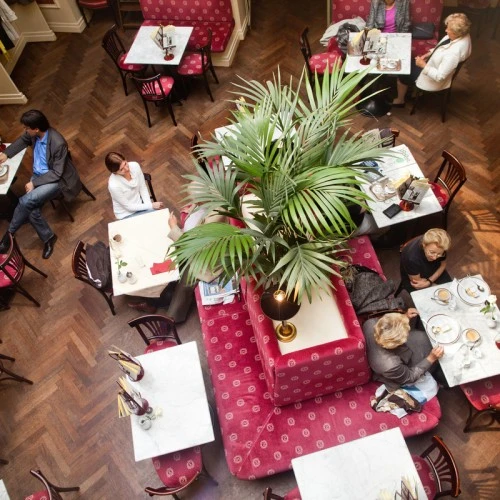 Gemütliches Kaffeehausambiente mit rot gepolsterten Bänken, Marmortischen und dunklem Holzparkett