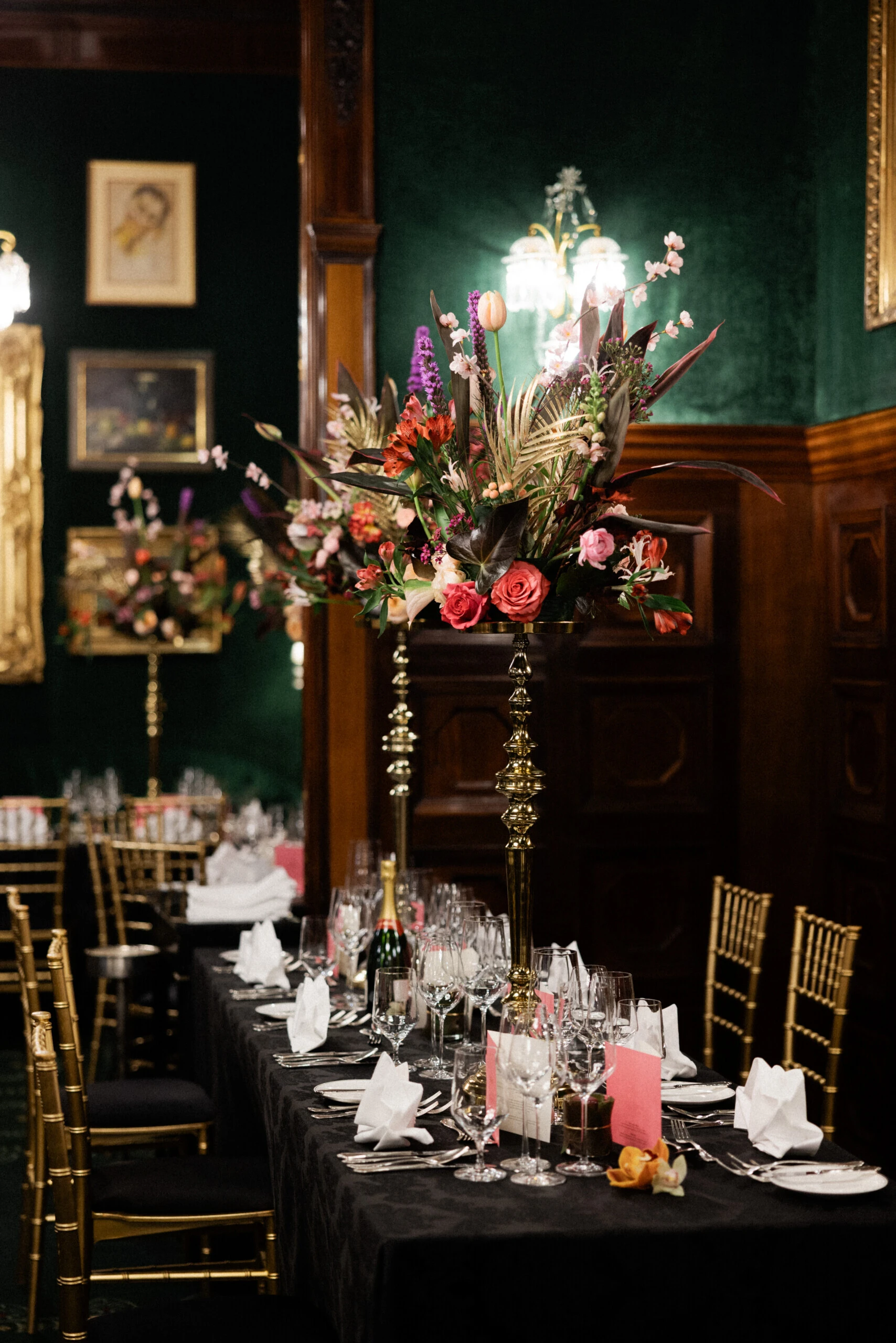 Festlich gedeckte Tafel im Restaurant Grüne Bar im Hotel Sacher Wien mit hohen Blumenarrangements und goldenen Stühlen.