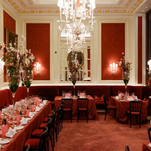 Festlich gedeckter Bereich im Café Sacher Wien mit roten Samtbänken, Kristallluster und hohen Blumenarrangements.