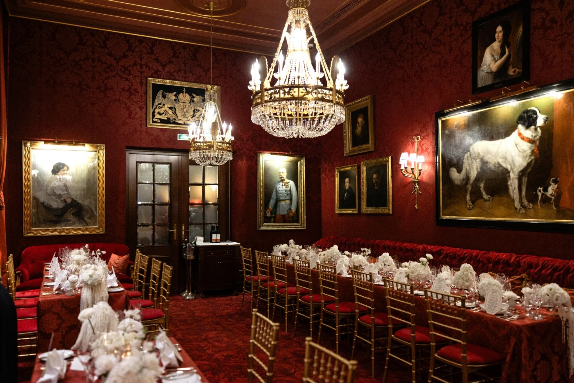 Festlich gedecktes Restaurant Rote Bar im Hotel Sacher Wien mit Kristalllüstern, roten Samtbänken, goldenen Stühlen und weißen Blumenarrangements.