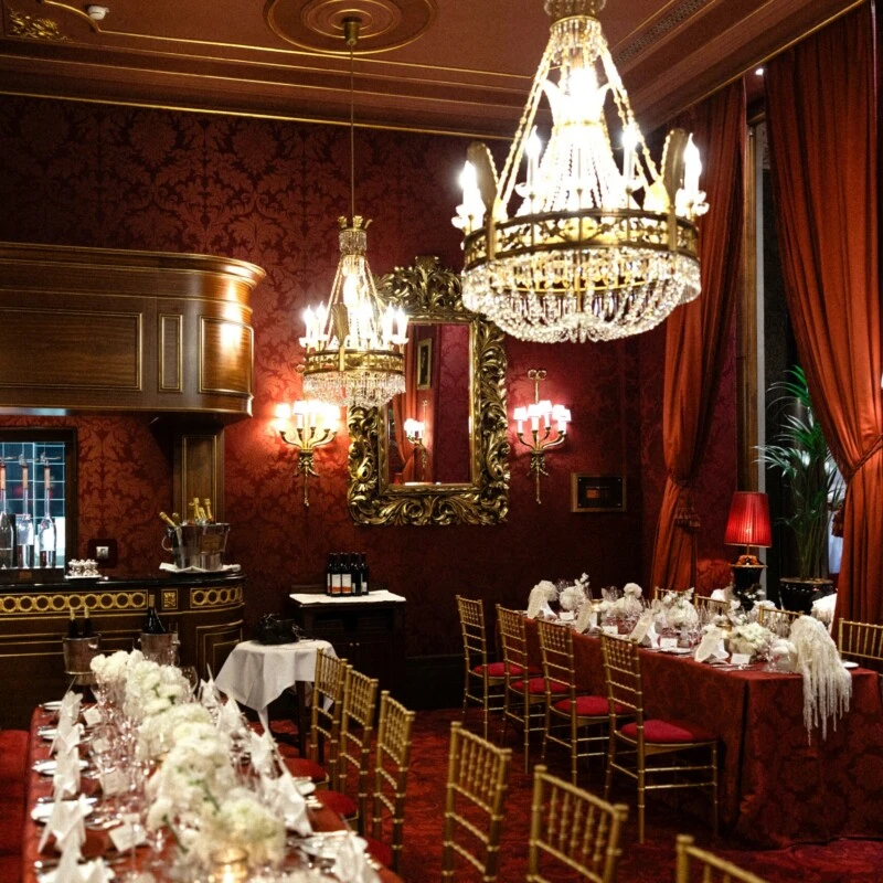 Festlich gedecktes Restaurant Rote Bar im Hotel Sacher Wien mit Kristalllüstern, roten Samtbänken, goldenen Stühlen und weißen Blumenarrangements.